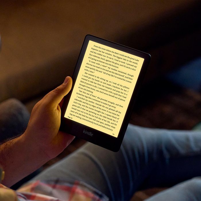 A person holds a Kindle, reading a passage illuminated on the screen, while seated in a cozy, dimly lit environment.