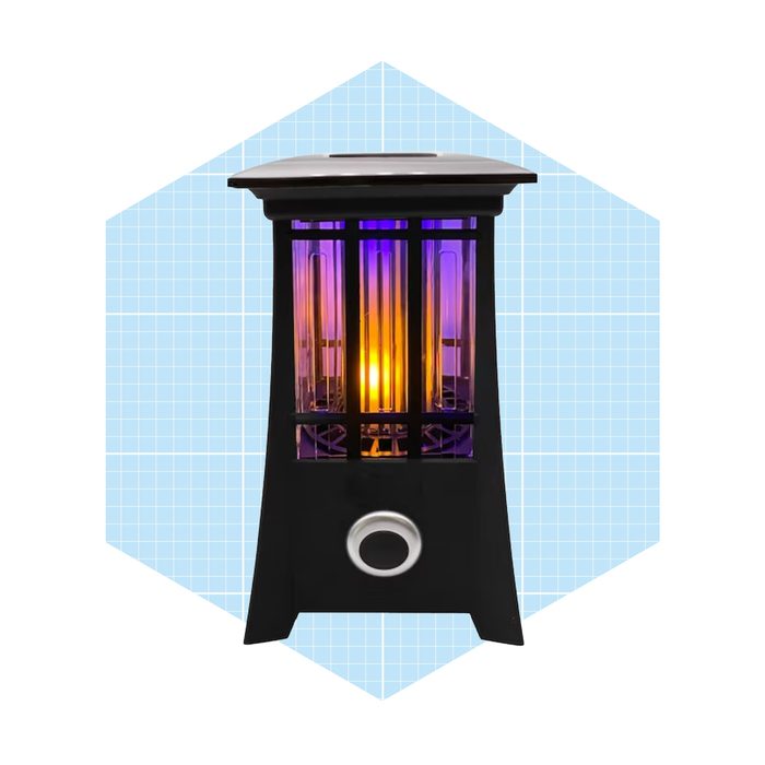 A black electric heater emits warm, colorful light. It stands upright against a soft blue geometric background, suggesting indoor use.