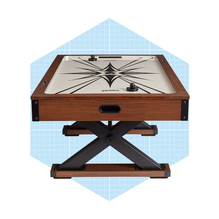 A wooden air hockey table with a black and white design on the surface sits on a sturdy, cross-shaped metal base against a light blue background.