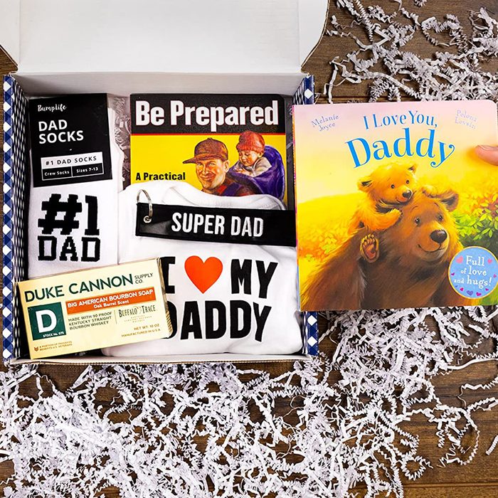 A gift box contains dad-themed items: socks labeled "#1 DAD," a T-shirt stating "I ?? MY DADDY," a practical book, and a children