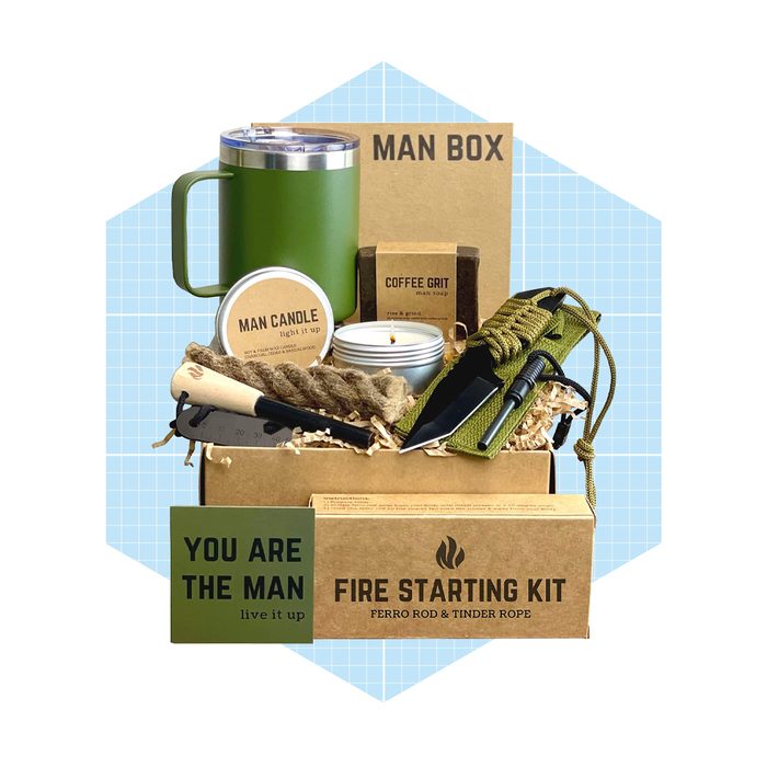 A green mug and gift box filled with various products, including candles, soap, a knife, and a fire-starting kit, set against a light blue background.