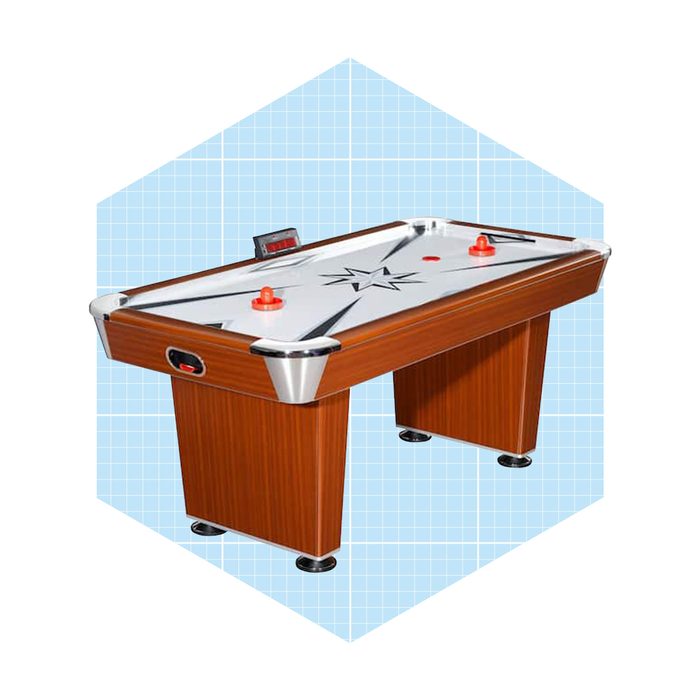 A wooden air hockey table with a silver playing surface and red pucks sits against a light blue grid background, suitable for recreational play.