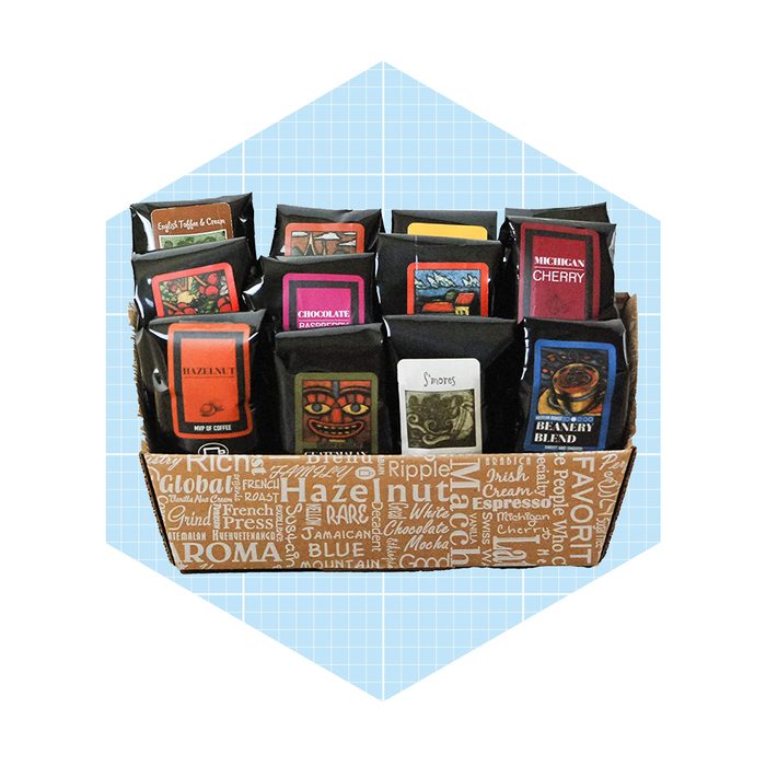 A box displays various coffee packages, each labeled with unique flavors, arranged neatly in rows against a light, patterned background.