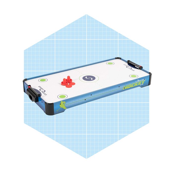 A tabletop air hockey game features a smooth surface with goals, red pucks, and scoring markers, set against a light blue grid background.