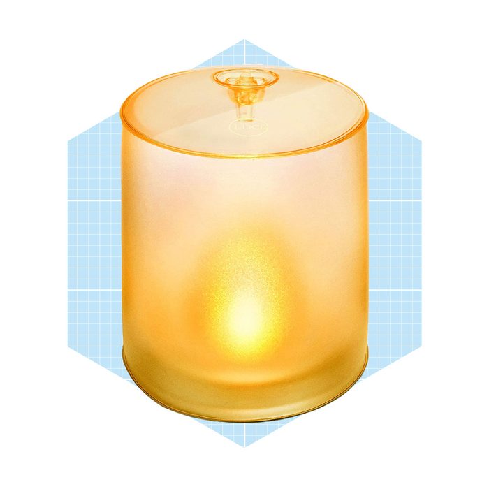 A translucent orange lantern emits a warm glow, situated against a light blue geometric background, giving a soft, inviting ambiance.