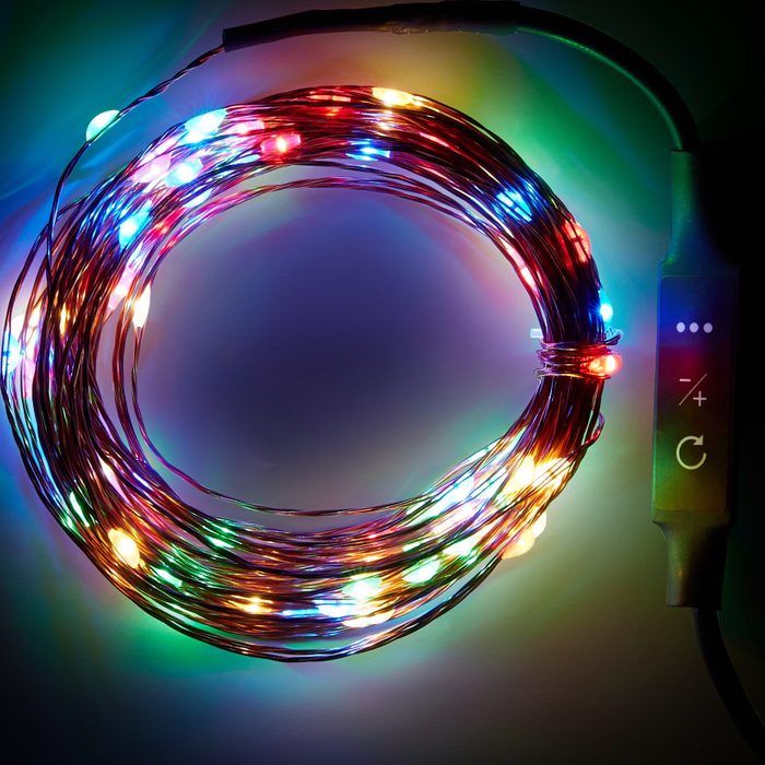 A circular strand of multicolored fairy lights glows brightly, coiled, with a control box attached for adjusting brightness, set against a dark background.