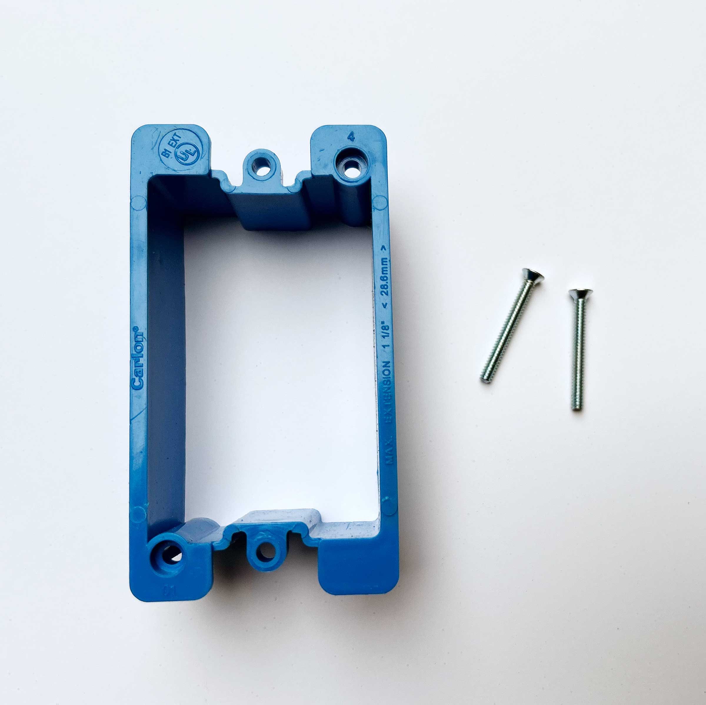 A blue electrical box sits on a white surface, with two metal screws beside it. The box has openings for wiring and mounting.
