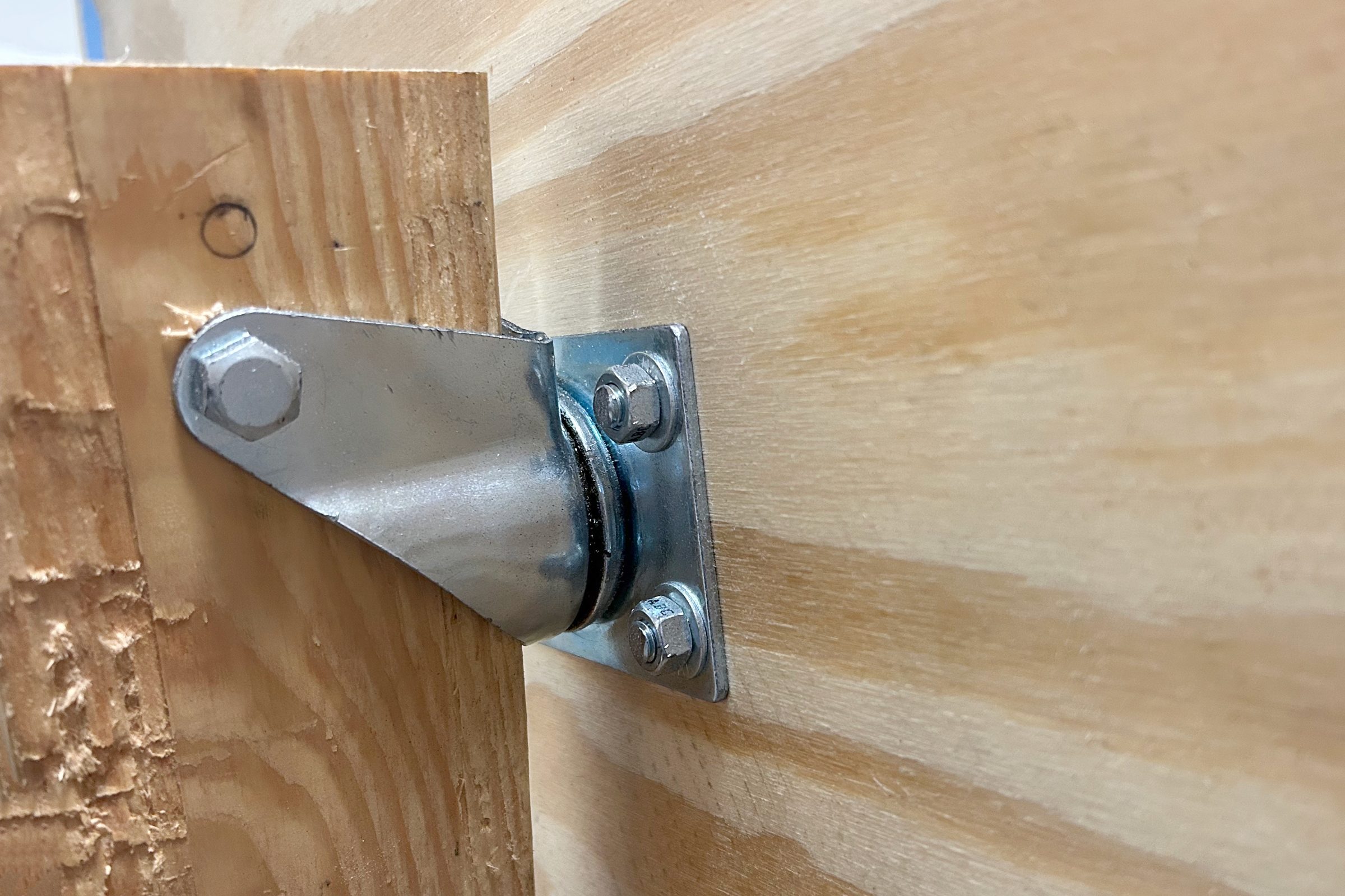 A metal hinge is attached to a wooden plank, facilitating movement between two wooden surfaces in a workshop setting.