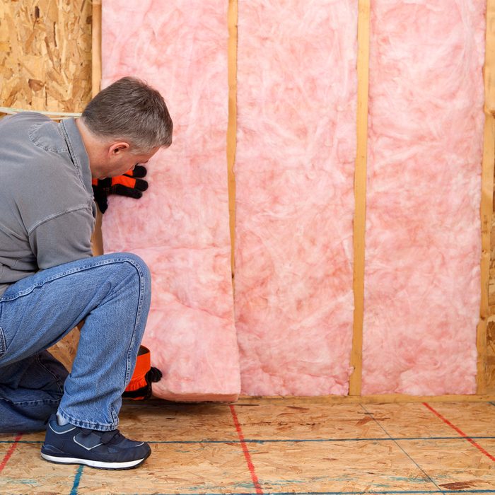 A person installs pink insulation between wooden studs in a room. They