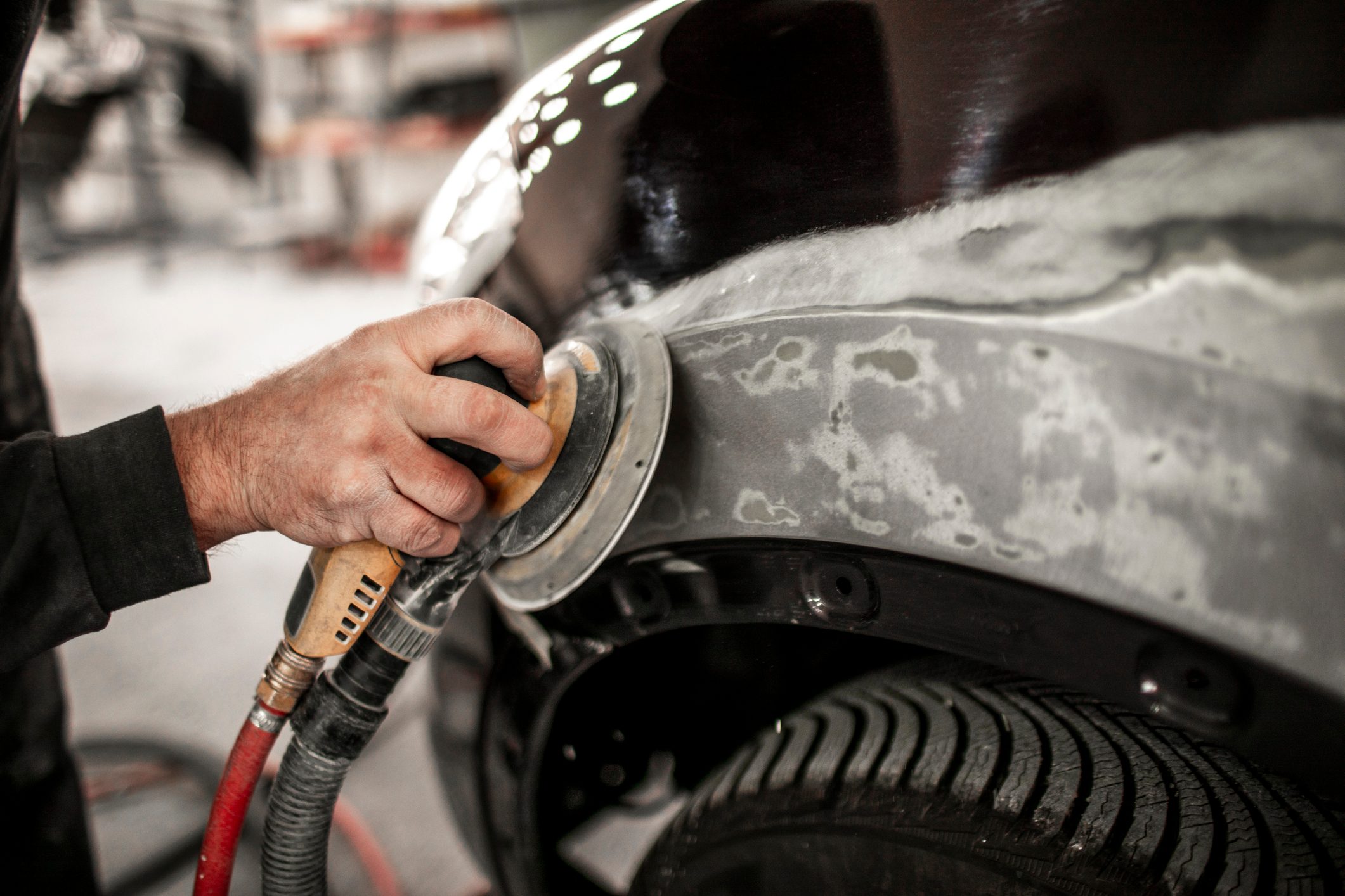 Using a portable electric sander to sand off damaged paint from a car quarter panel