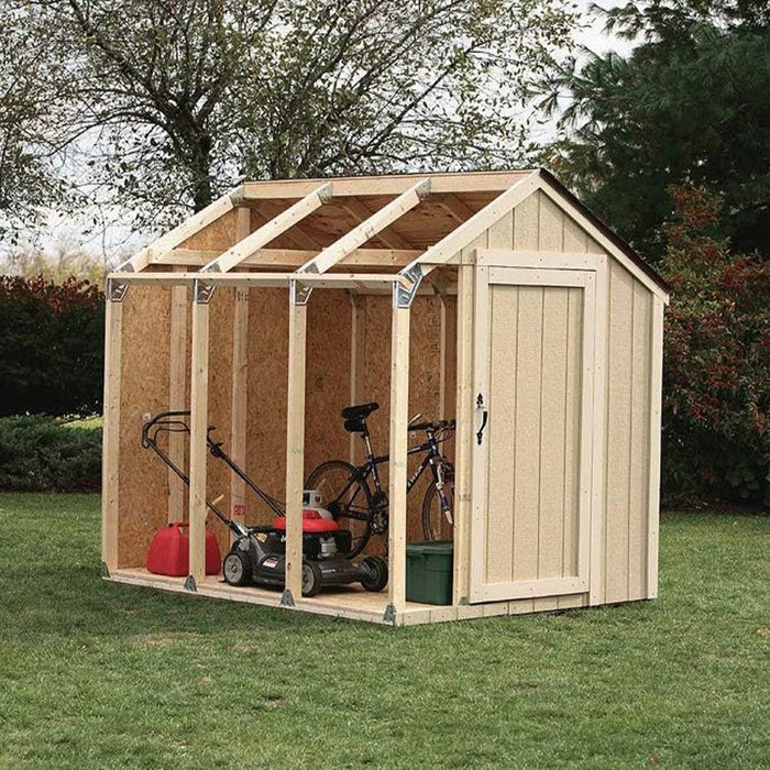 A wooden shed stores a bicycle, lawnmower, and gas cans, positioned on grass under trees, with its sides partially open.