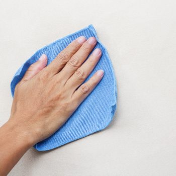 A hand wipes a smooth surface with a blue cloth, cleaning a light-colored area as part of a cleaning task.