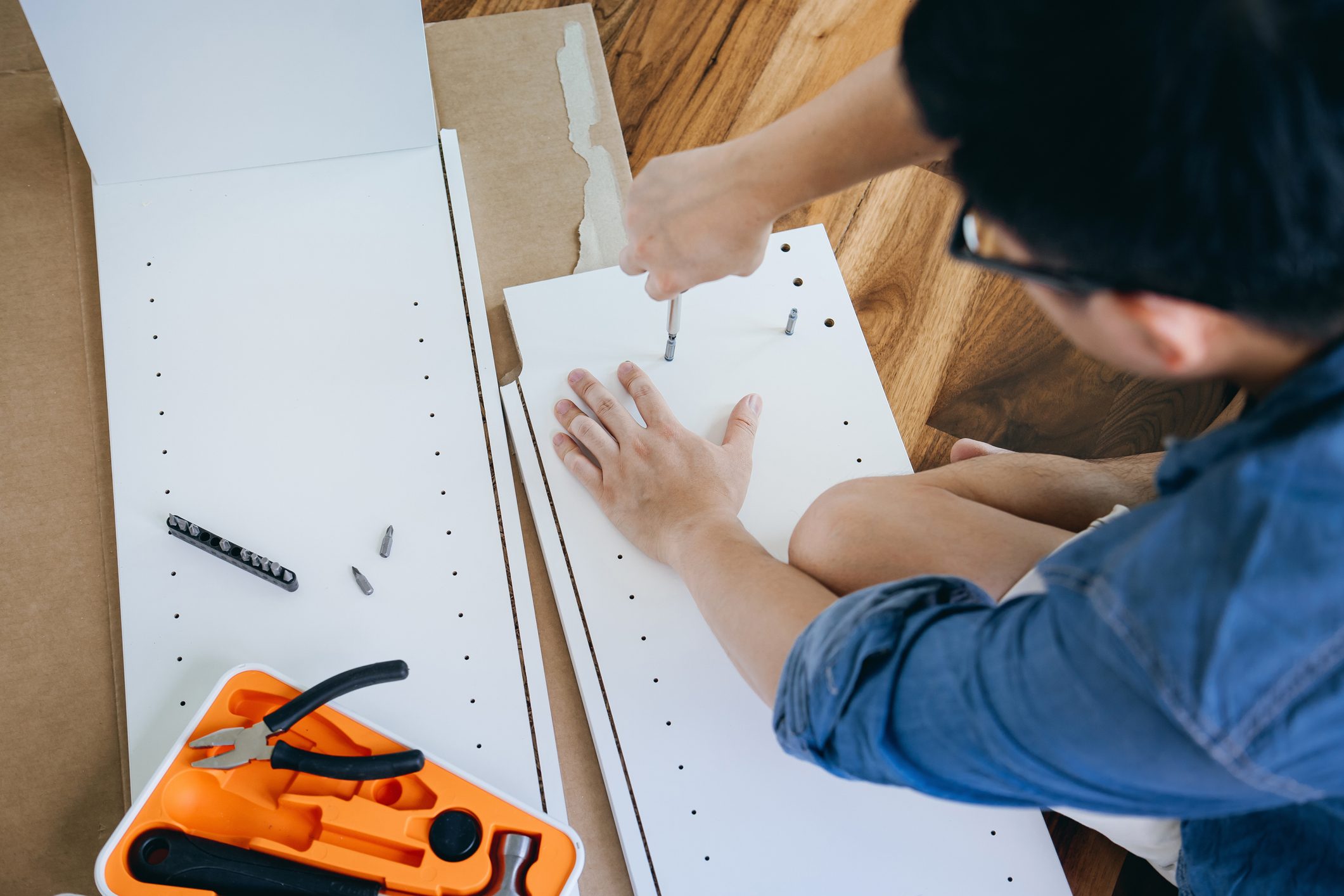High angle shot of young Asian man assembling furniture with a screwdriver. He is assembling a wooden cabinet in the living room in his new apartment