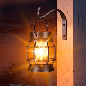 A hanging lantern emits a warm glow, illuminating a wooden wall in a cozy, dimly lit outdoor setting, with brick and greenery visible in the background.
