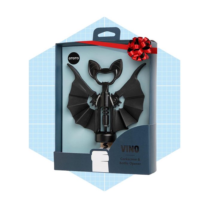 A bat-shaped corkscrew and bottle opener is displayed in a decorative box with a bow, set against a light blue grid background.