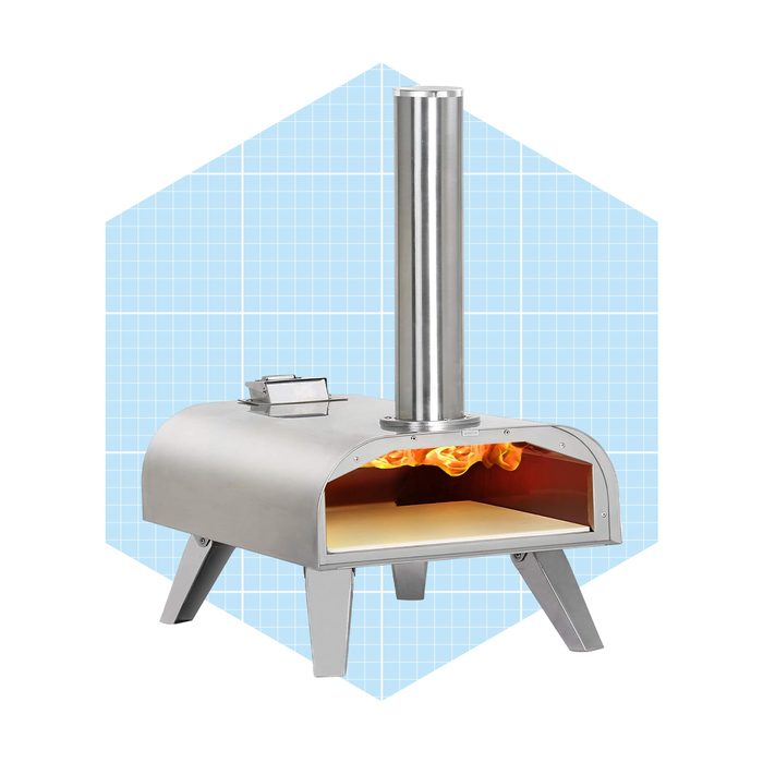 A metallic outdoor oven emits flames inside, preparing to cook. It features a chimney and stands on four legs, set against a light blue backdrop.