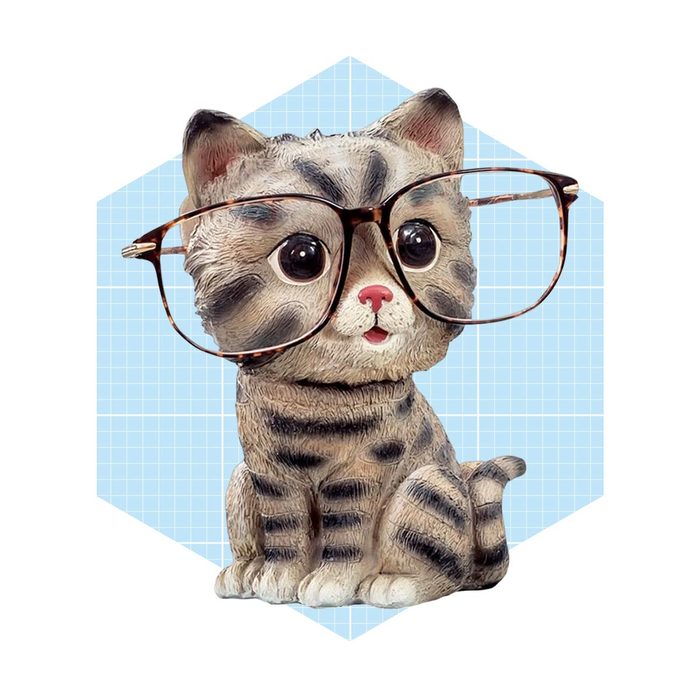 A small, decorative cat figurine wearing large glasses sits against a light blue geometric background, exuding a whimsical, endearing charm.