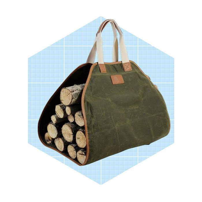 A green fabric bag filled with neatly stacked logs is displayed against a light blue grid background, showcasing its sturdy structure and dual handles.