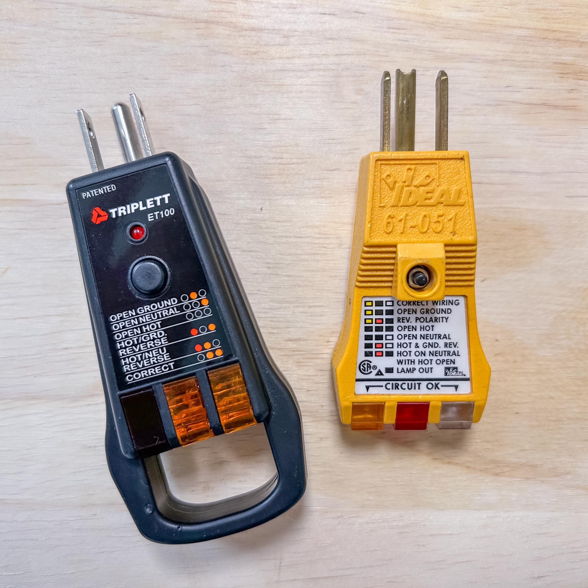 Two electrical testers, one black and one yellow, are displayed on a light wooden surface, indicating various electrical conditions and wiring statuses.