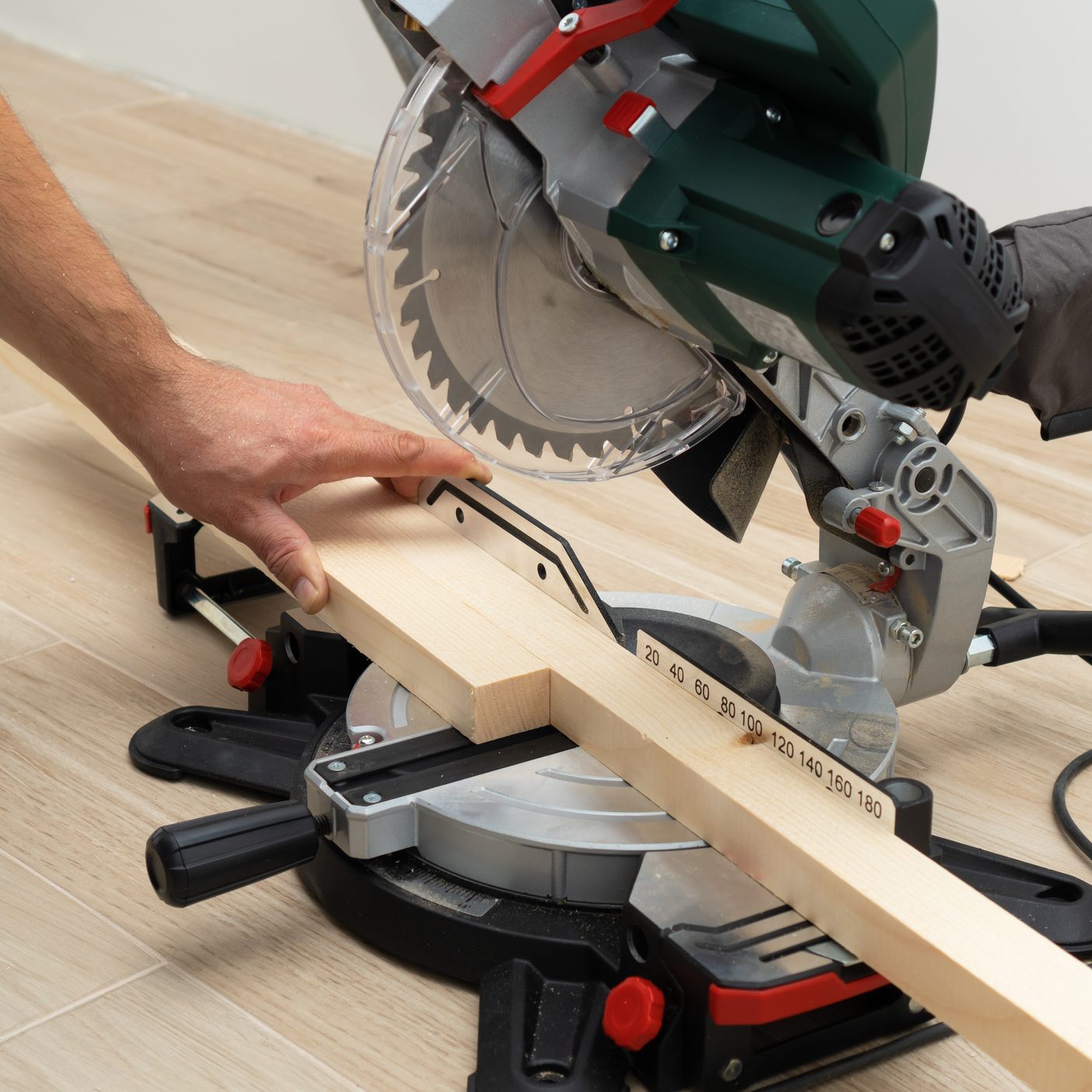 Power tool miter saw in hands of a handyman sawing wood parts.