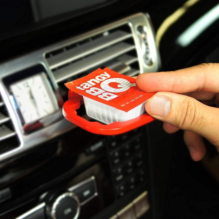 A hand holds a red condiment container while placing it near a car
