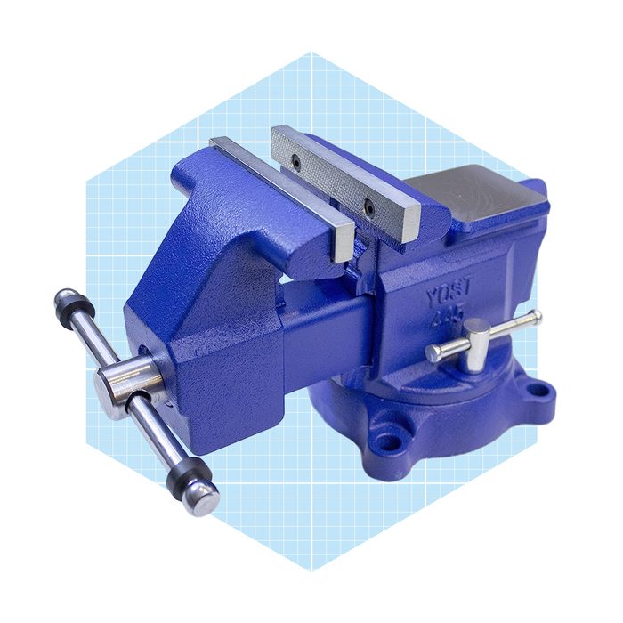A blue metal vise sits on a light blue geometric background, featuring parallel jaws designed to hold objects securely during work.