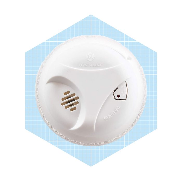 A white smoke detector sits above a blue grid background, designed for safety with vents and a test button, ensuring fire alert functionality.