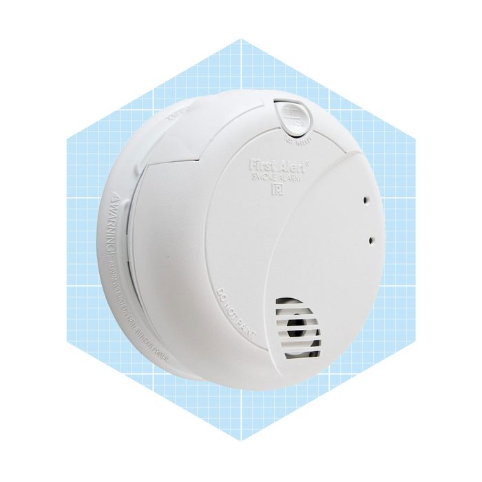 A white smoke alarm hangs against a light blue grid background, designed to detect smoke and alert occupants to danger.
