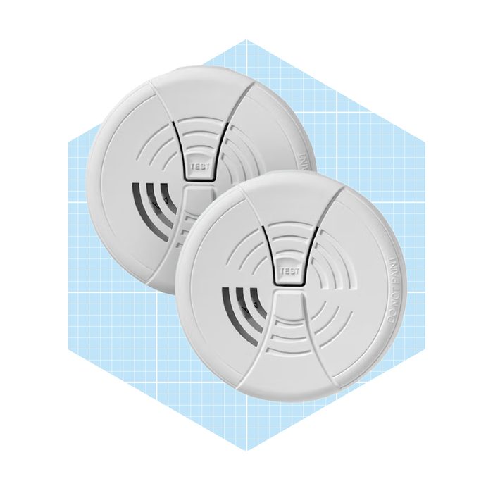 Two white smoke detectors are displayed, positioned next to each other, on a light blue hexagonal background with a grid pattern.