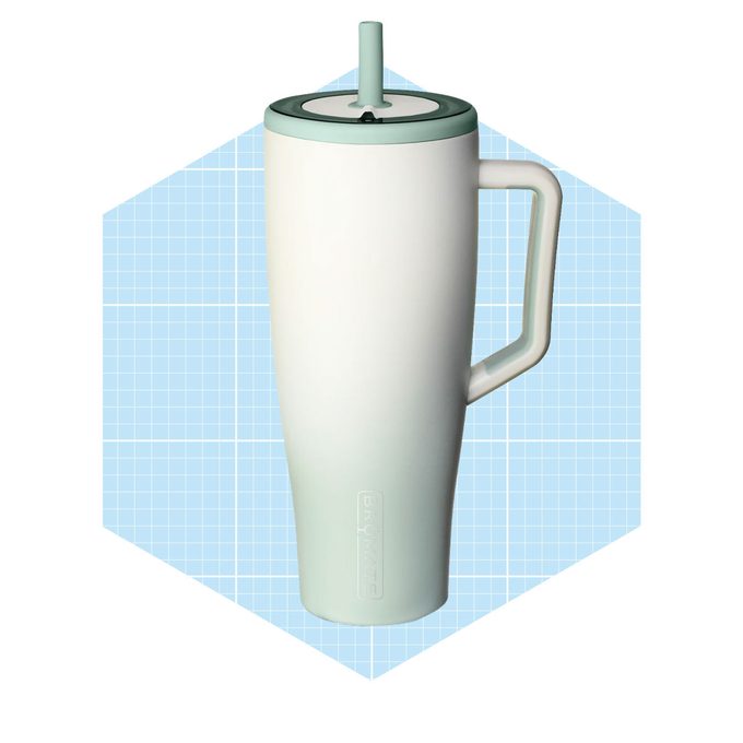 A tall, curved mug with a handle and a lid featuring a straw rests against a light blue grid background.