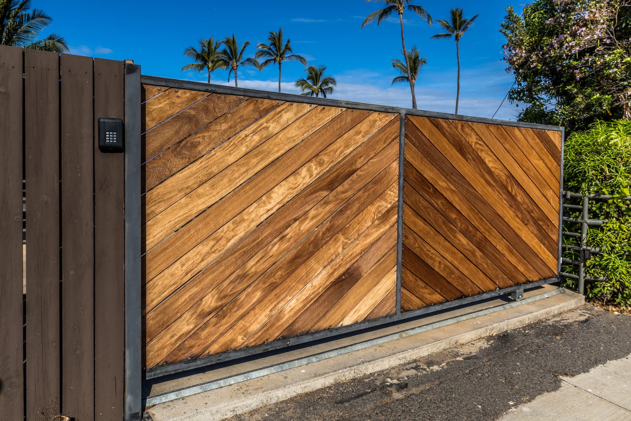 Stained natural wood modern and clean wood driveway property private gate entrance in a tropical location with secure gate access pinpad