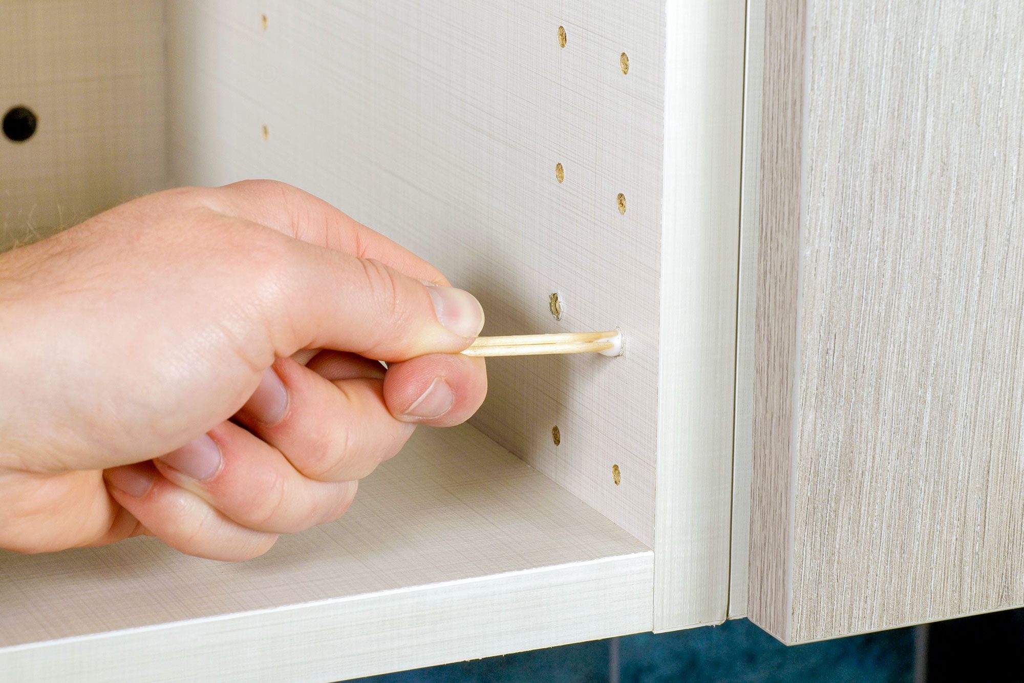 Inserting toothpicks into a hole in wooden cabinet
