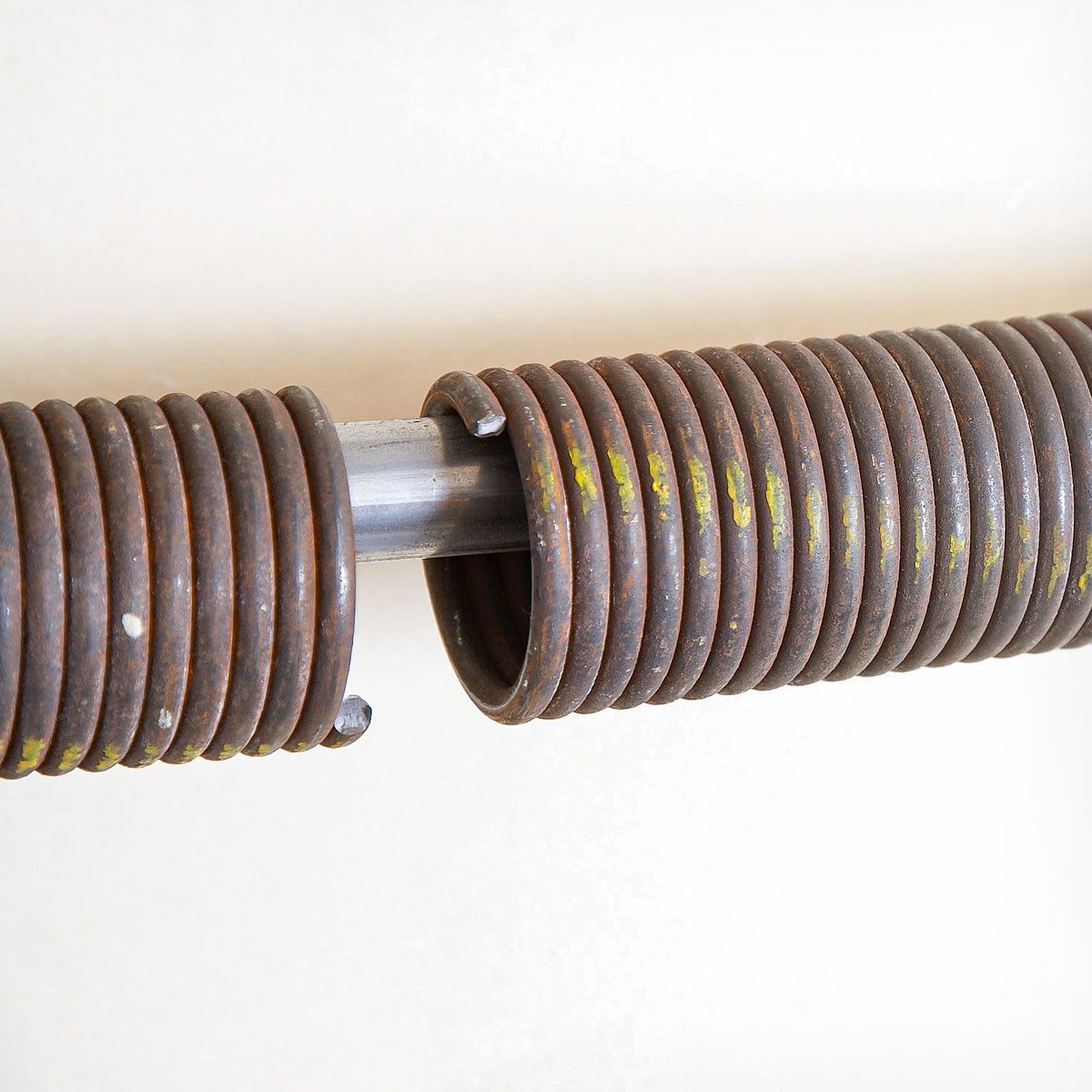 Coiled metal springs connect on a metal shaft, appearing worn and rusted. They are set against a light, neutral background, emphasizing their texture and condition.