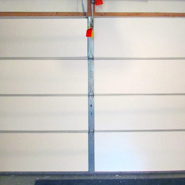 A closed garage door, featuring horizontal grooves and metallic hinges, stands against a plain background in a well-lit indoor environment.