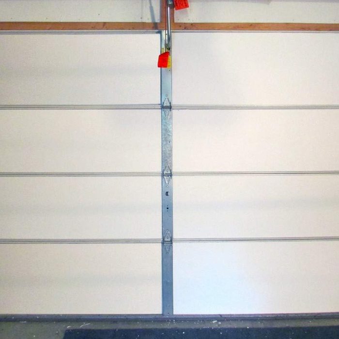A closed garage door, featuring horizontal grooves and metallic hinges, stands against a plain background in a well-lit indoor environment.
