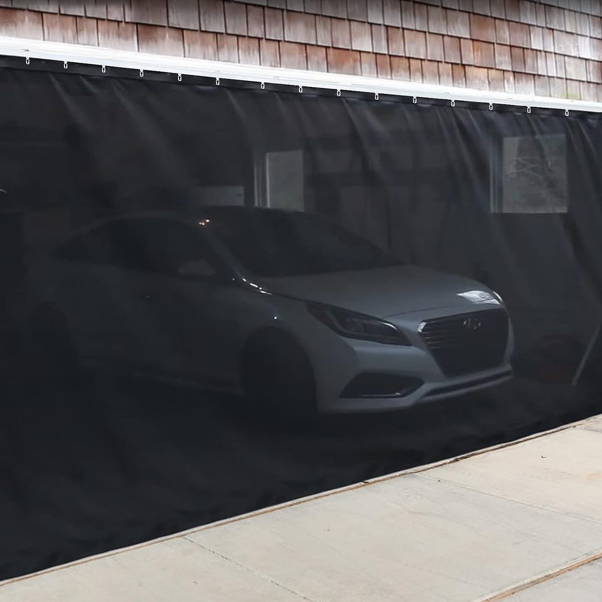 A white car is parked behind a black curtain in a garage with wooden siding, creating a secluded atmosphere.