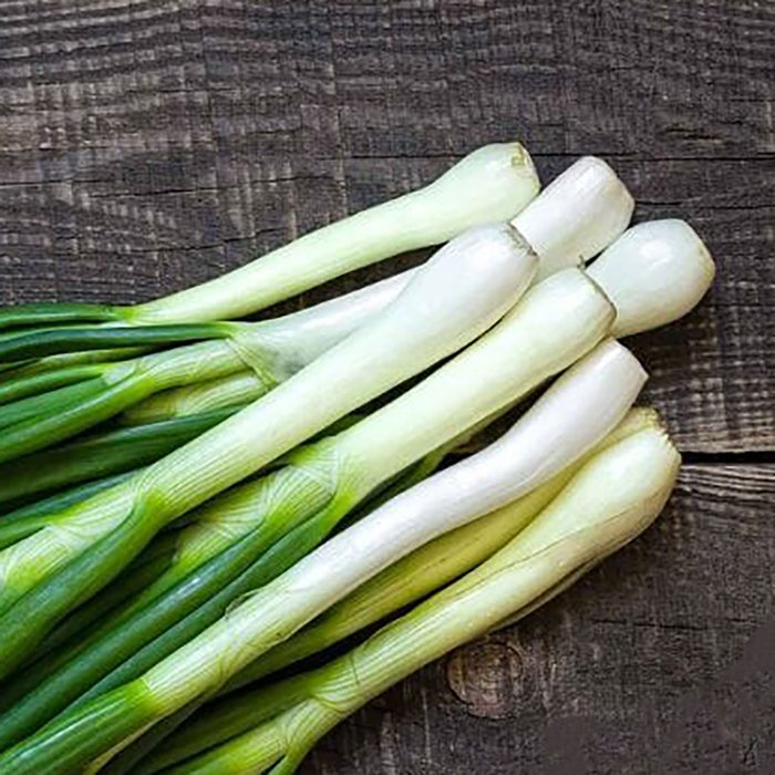 Fresh green onions lie parallel on a wooden surface, showcasing their long green tops and white bulbs, ready for culinary use.