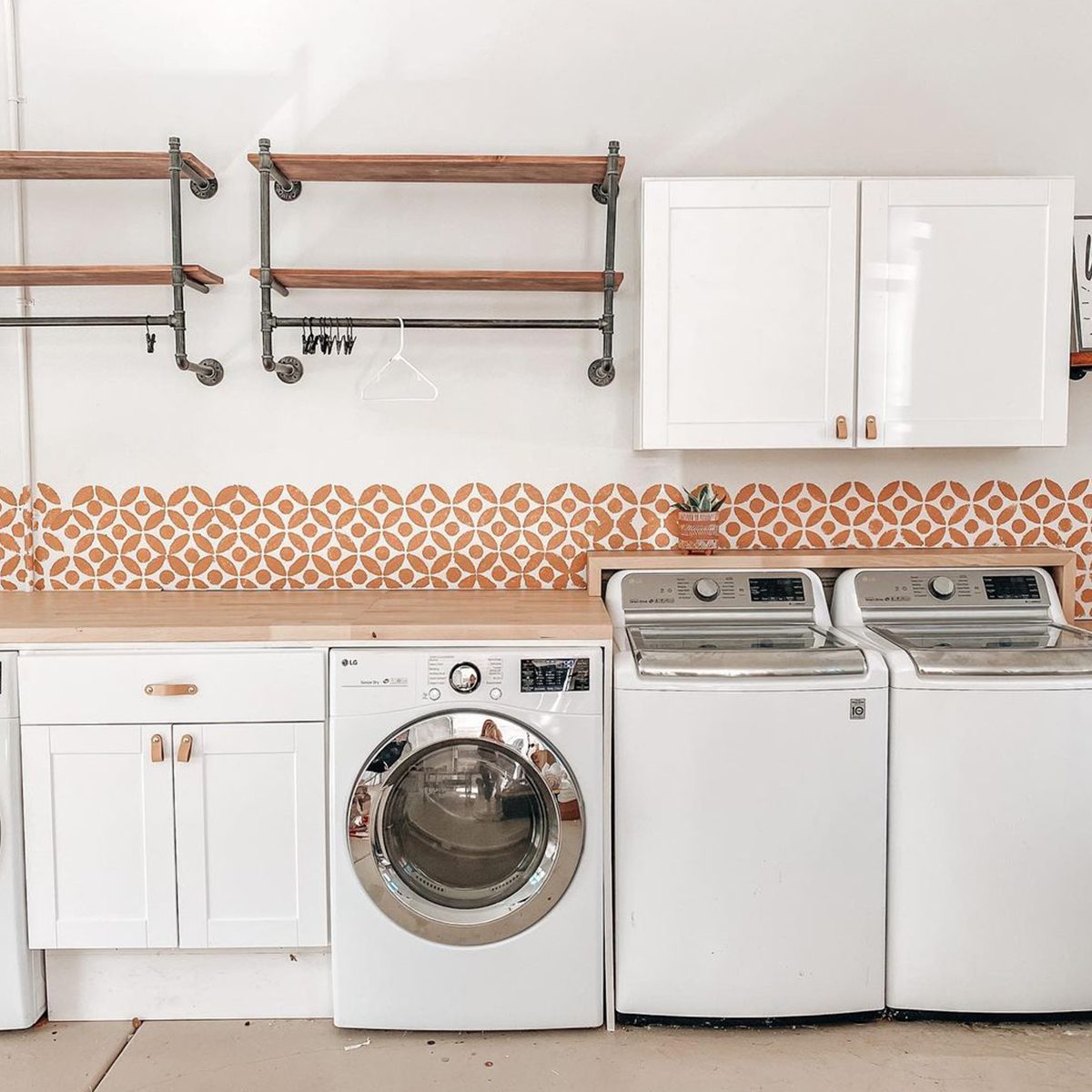 A washing machine and dryer sit side by side on a countertop, under shelves with a patterned backsplash. The area appears organized and modern.