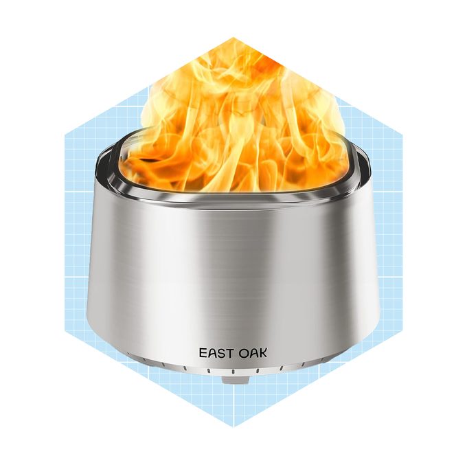 A stainless steel fire pit emits vibrant flames, surrounded by a light blue grid background, suggesting an outdoor or cozy environment. Text reads "EAST OAK."