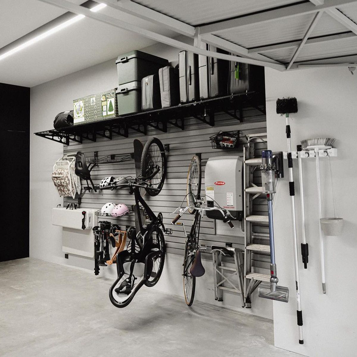 A black bike and several tools are hung on a gray wall; organized items include storage boxes, helmets, and cleaning equipment in a spacious garage.