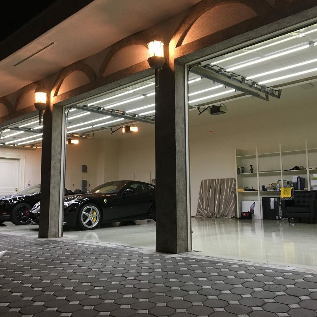 A black sports car sits in a well-lit garage, surrounded by clean concrete and shelves, under bright fluorescent lights.