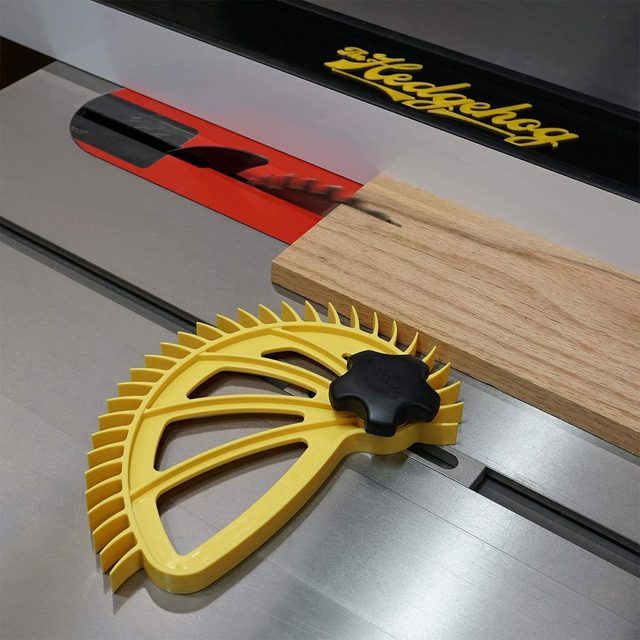A yellow push stick rests beside a piece of wood on a table saw, indicating preparation for cutting with the blade partly visible.