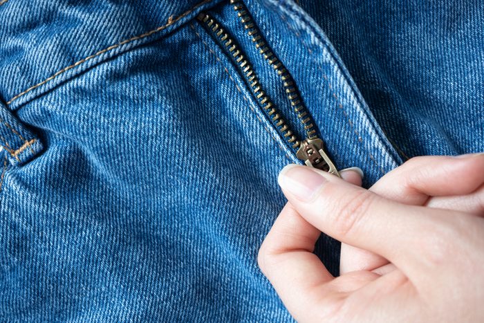 Hand open metal zipper on fly blue jeans