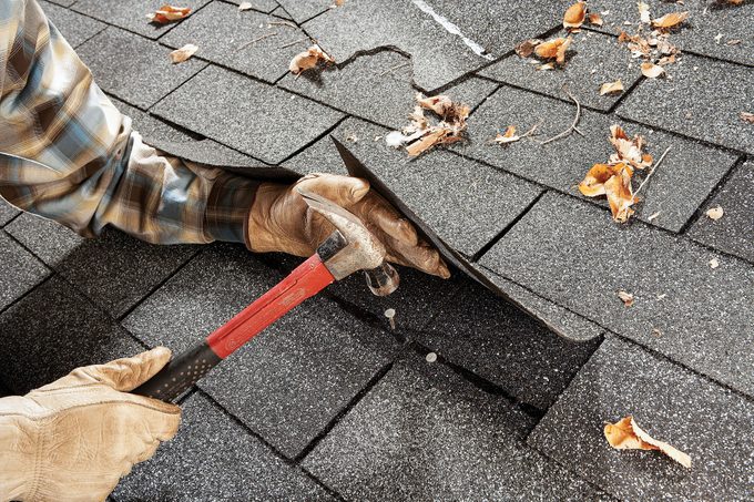 a person hammering a nail on shingles
