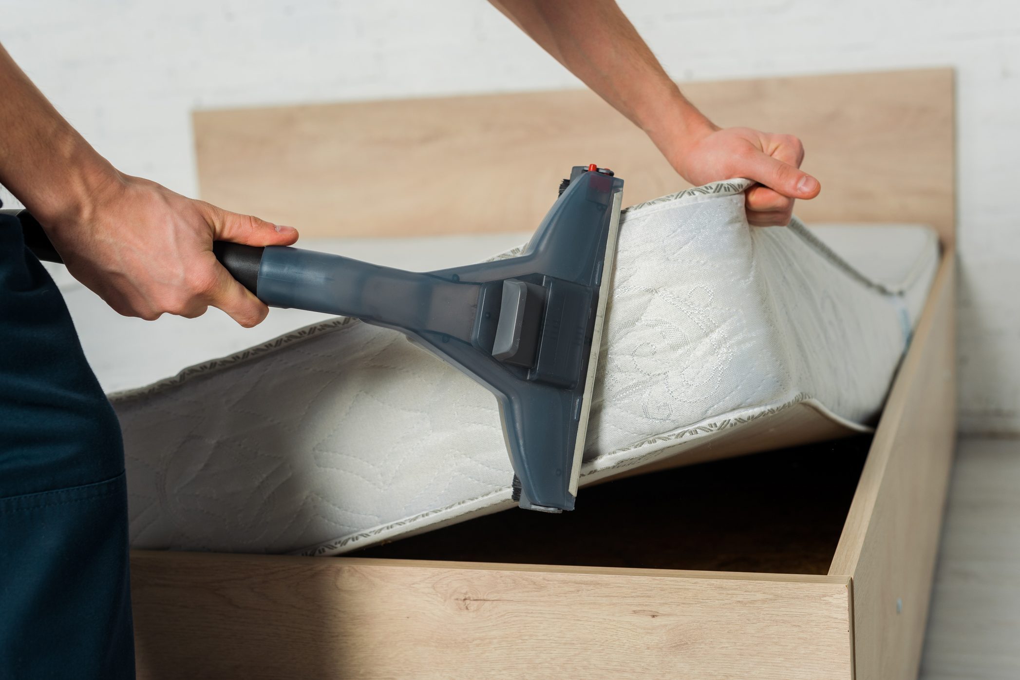 Man removing dust from mattress with vacuum cleaner