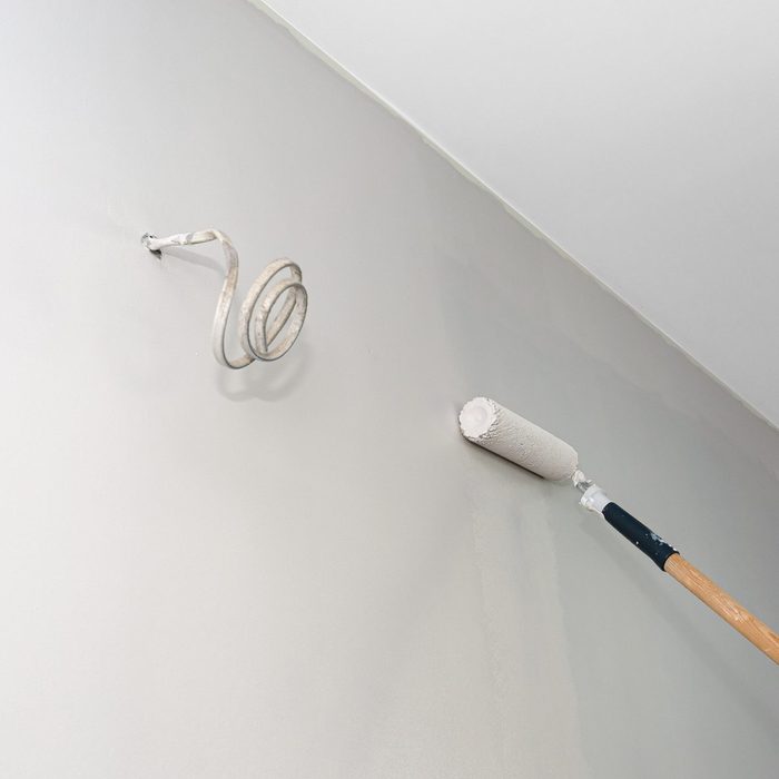 Painter paints a room in beige color using a paint roller on an extended stick at home.
