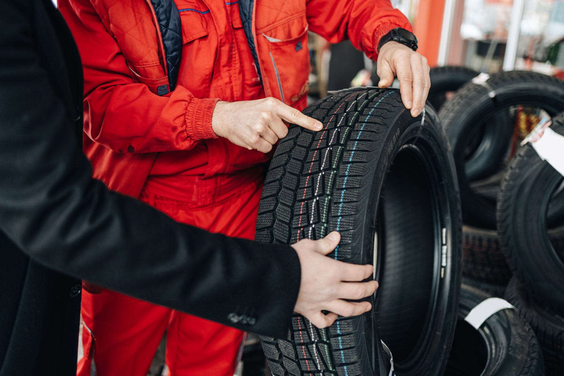 Young customer looking for some good new winter tires. He is talking with salesman and asking him for advice.