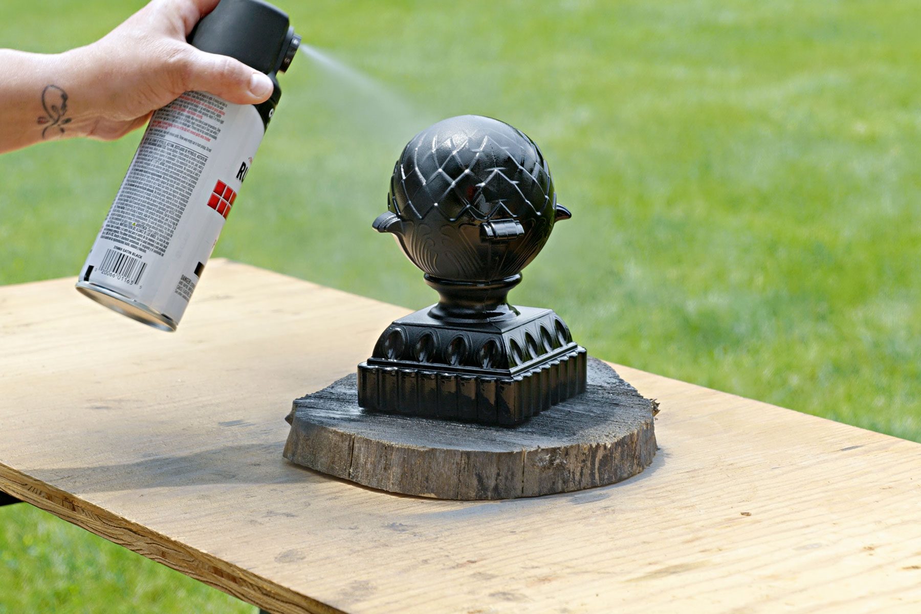 A hand can be seen painting the finial with spray paint from a can.