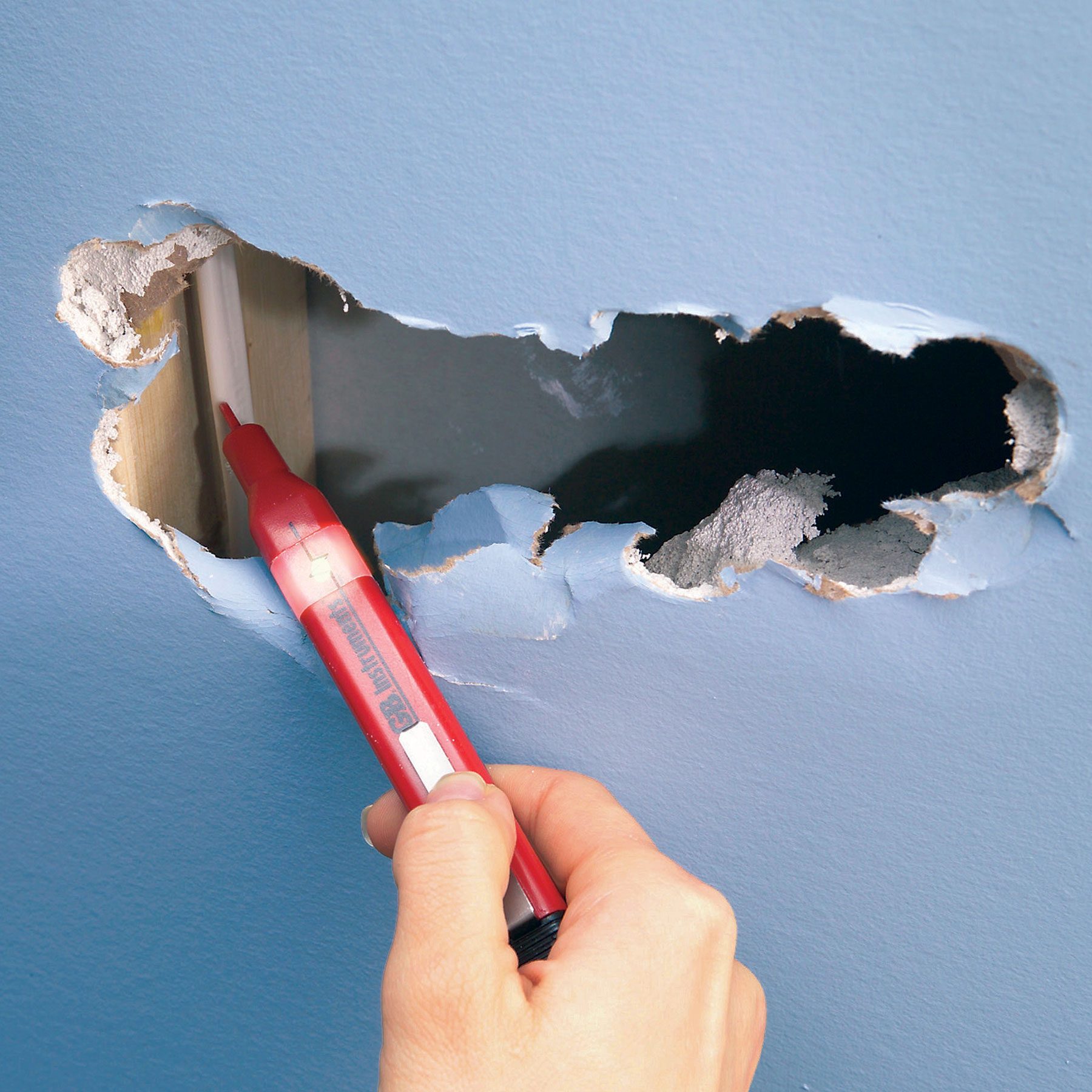 A hand can be seen using a non-contact voltage tester to determine whether or not electrical cables inside a wall are live.