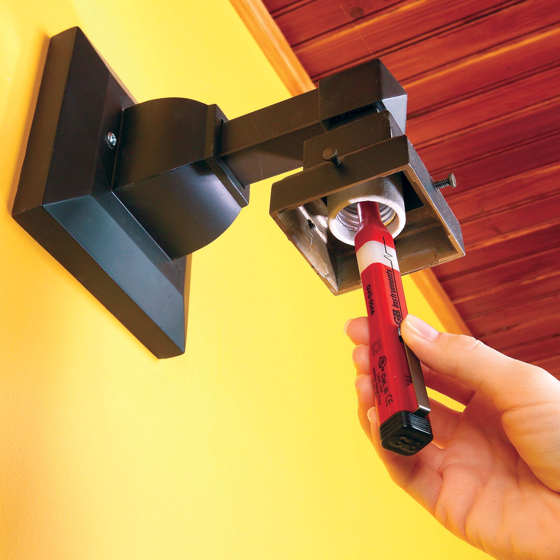 A hand can be seen using a non-contact voltage tester to check a light fixture.
